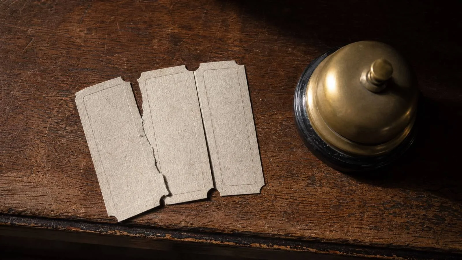 Three paper tickets on a worn wooden counter beside a brass bell push