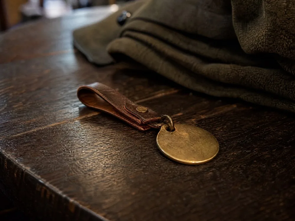 A brass cloakroom tag on a leather loop beside a folded coat