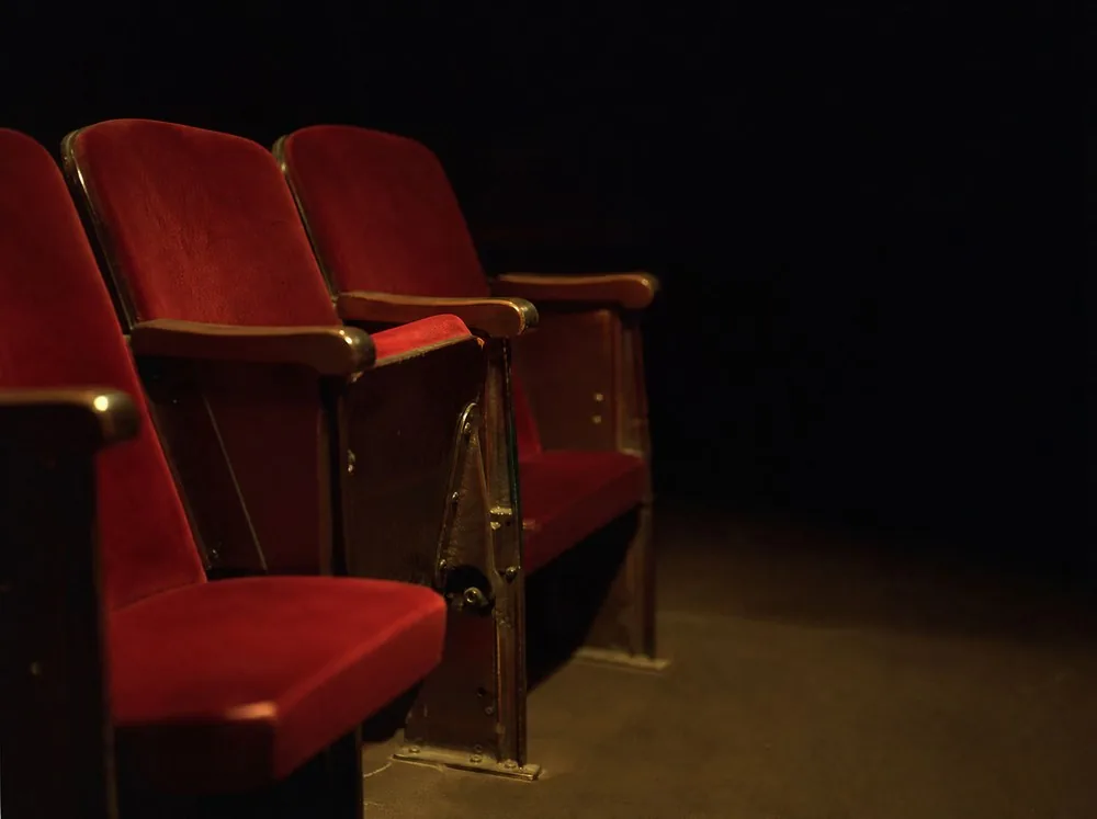 A short row of empty red velvet seats in a dim auditorium